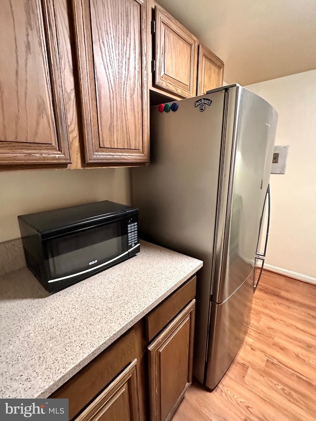 kitchen with baseboards, brown cabinets, light wood finished floors, and freestanding refrigerator