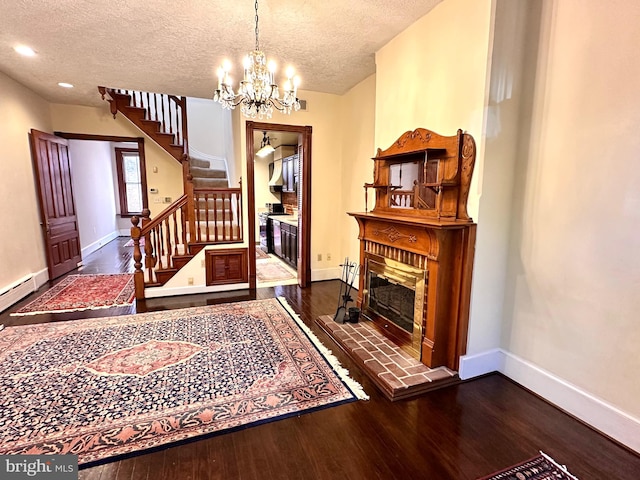 foyer entrance featuring dark wood-type flooring, a brick fireplace, a textured ceiling, and an inviting chandelier