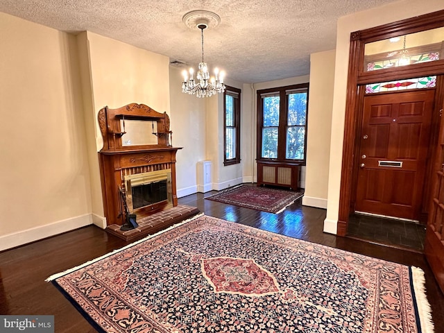 foyer entrance with a textured ceiling, a chandelier, wood finished floors, and baseboards