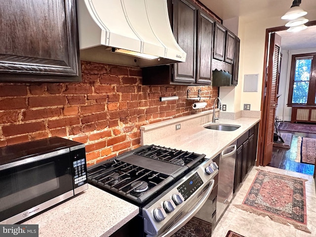 kitchen with dark brown cabinetry, light stone countertops, stainless steel appliances, a sink, and ventilation hood