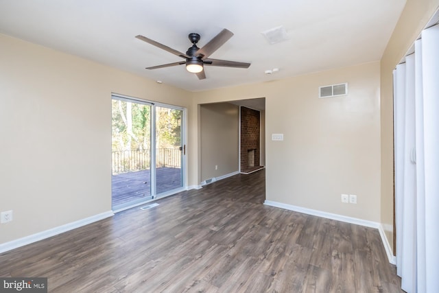 empty room with ceiling fan, a brick fireplace, and dark hardwood / wood-style floors