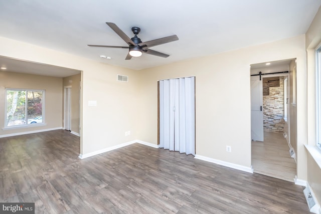 unfurnished room with ceiling fan, a barn door, and hardwood / wood-style floors