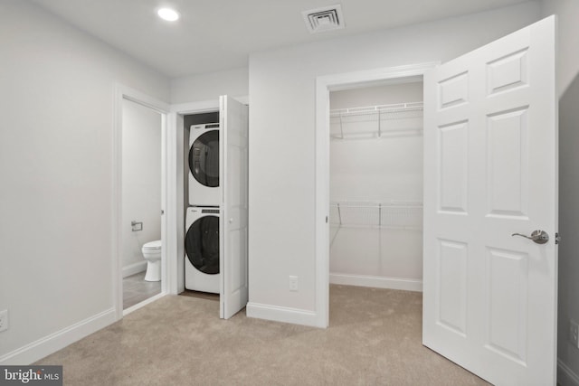 laundry area featuring stacked washing maching and dryer and light carpet