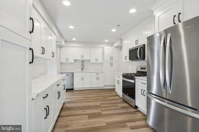 kitchen with light stone counters, stainless steel appliances, white cabinetry, sink, and light hardwood / wood-style flooring