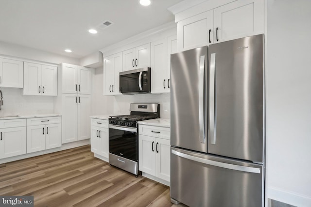 kitchen with white cabinets, light wood-type flooring, and appliances with stainless steel finishes