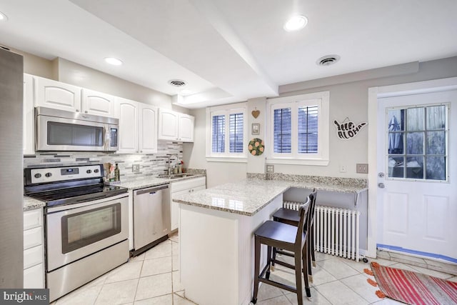 kitchen with white cabinetry, sink, radiator heating unit, a kitchen bar, and appliances with stainless steel finishes