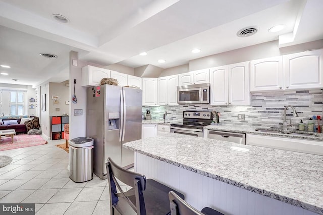 kitchen with light stone countertops, sink, stainless steel appliances, tasteful backsplash, and white cabinets