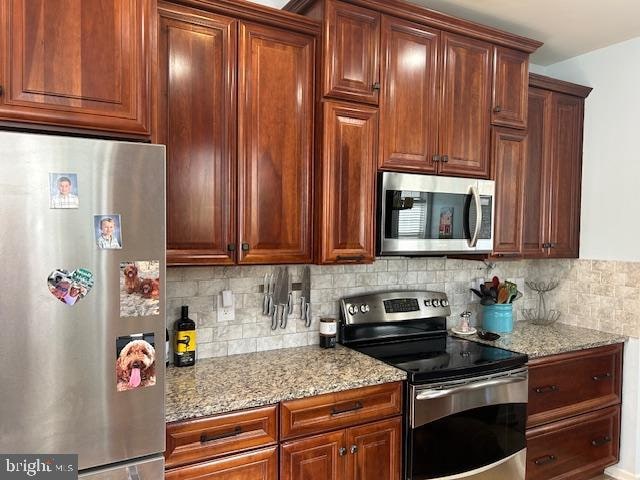 kitchen with appliances with stainless steel finishes, light stone counters, and tasteful backsplash