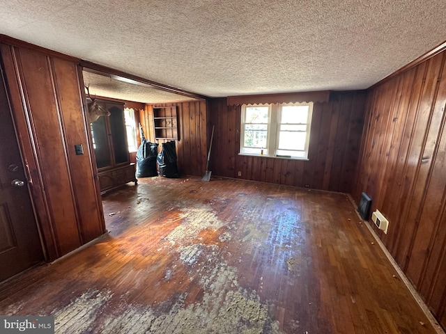 interior space with wood walls, a textured ceiling, and dark wood-type flooring