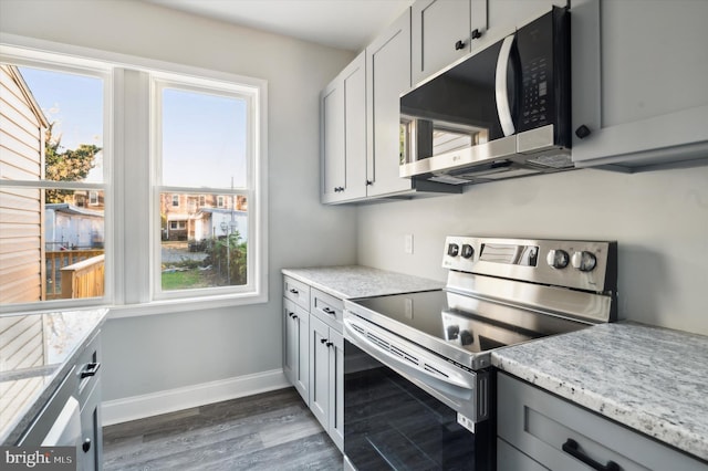 kitchen featuring appliances with stainless steel finishes, a healthy amount of sunlight, light stone counters, and dark wood-type flooring