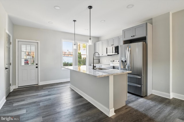 kitchen featuring light stone counters, appliances with stainless steel finishes, plenty of natural light, and an island with sink