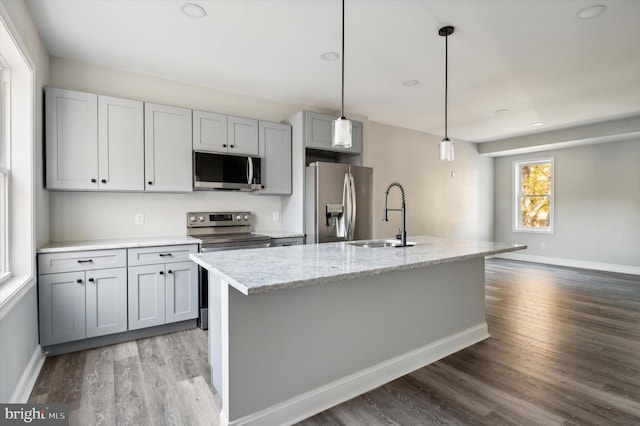 kitchen featuring light stone countertops, appliances with stainless steel finishes, sink, light hardwood / wood-style flooring, and a center island with sink