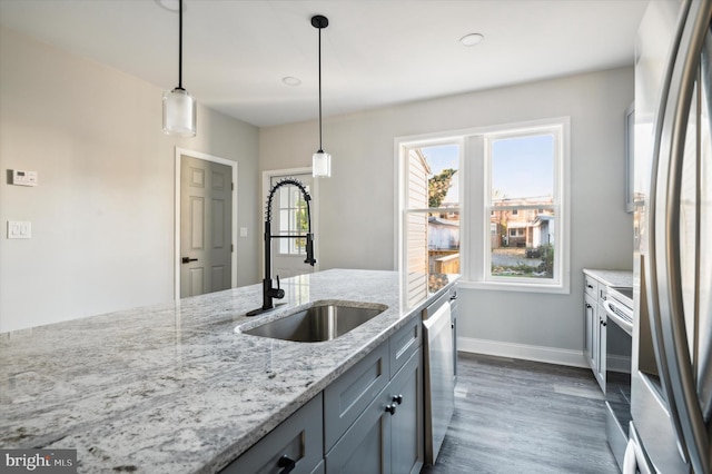 kitchen featuring light stone counters, dark hardwood / wood-style flooring, stainless steel appliances, sink, and decorative light fixtures