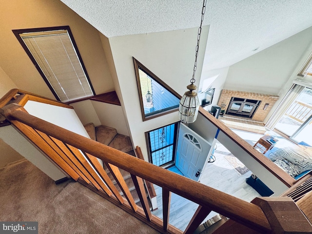 staircase with a textured ceiling, carpet floors, and a brick fireplace