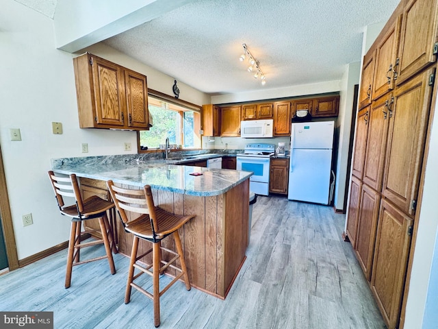 kitchen featuring a kitchen bar, kitchen peninsula, light wood-type flooring, and white appliances