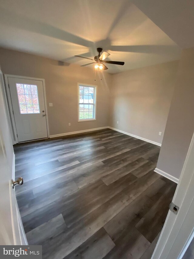 empty room with dark wood-type flooring, plenty of natural light, and ceiling fan