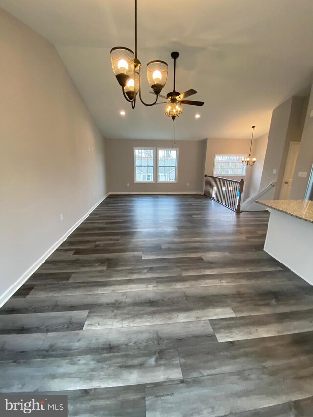 unfurnished dining area featuring vaulted ceiling, ceiling fan with notable chandelier, and dark hardwood / wood-style flooring