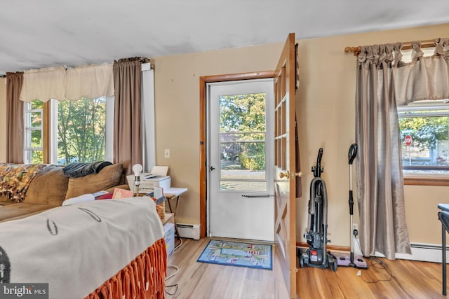 doorway with a baseboard heating unit, plenty of natural light, and wood finished floors