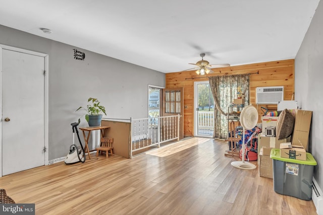 interior space featuring a wall mounted air conditioner, wooden walls, wood finished floors, and a ceiling fan