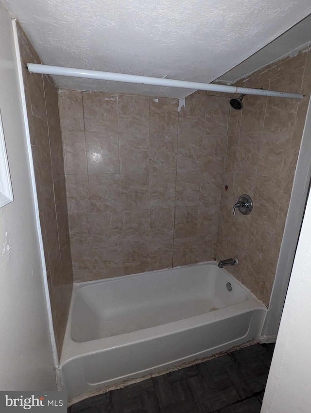 bathroom with a textured ceiling and tiled shower / bath