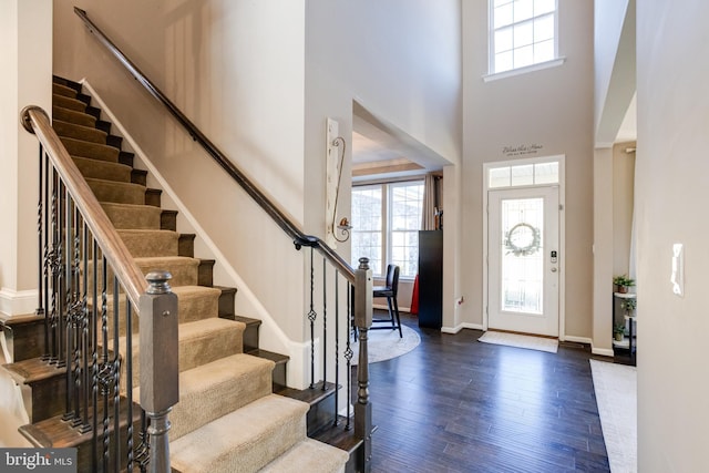 foyer entrance featuring a towering ceiling, a healthy amount of sunlight, and dark hardwood / wood-style flooring