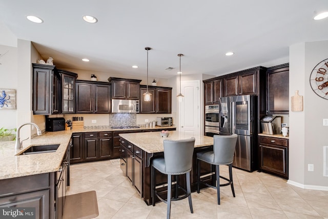 kitchen with a breakfast bar area, decorative light fixtures, a center island, dark brown cabinets, and appliances with stainless steel finishes