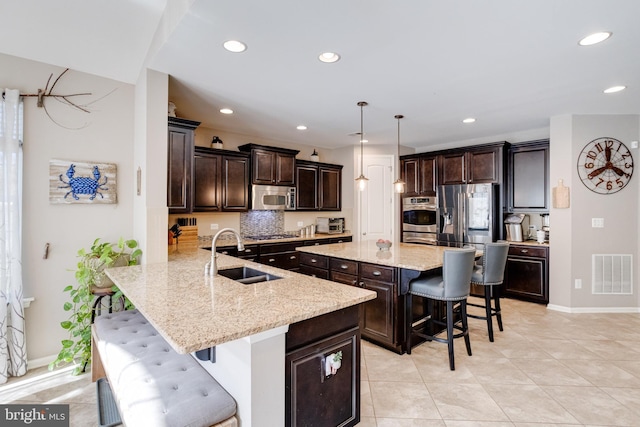 kitchen featuring sink, appliances with stainless steel finishes, hanging light fixtures, dark brown cabinets, and a kitchen breakfast bar