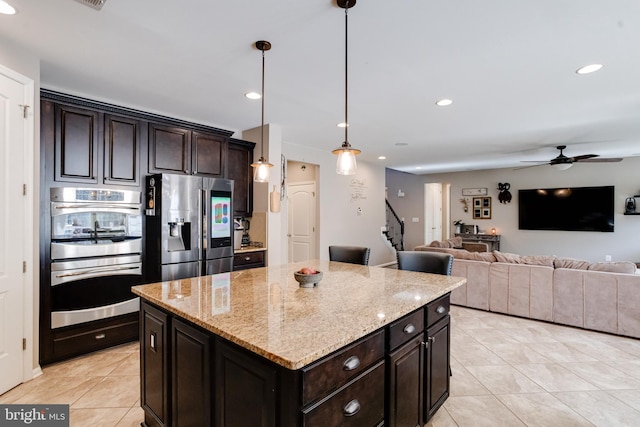 kitchen featuring dark brown cabinetry, a center island, pendant lighting, stainless steel appliances, and light stone countertops