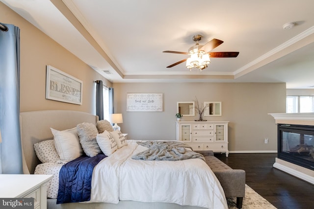 bedroom featuring dark hardwood / wood-style floors, a multi sided fireplace, ornamental molding, and a tray ceiling