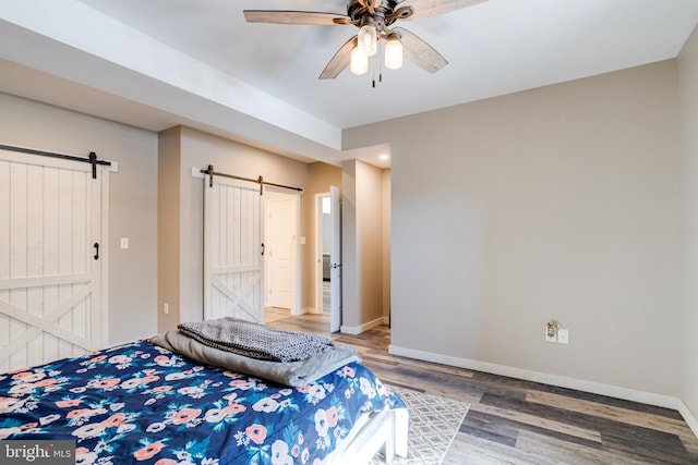 bedroom with hardwood / wood-style flooring, ceiling fan, and a barn door