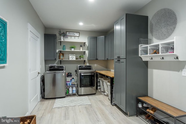 clothes washing area featuring washing machine and dryer, light hardwood / wood-style floors, and cabinets