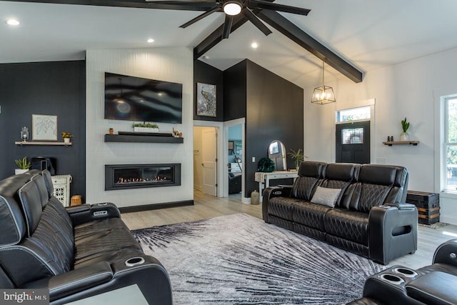 living room featuring light hardwood / wood-style floors, a large fireplace, vaulted ceiling with beams, and ceiling fan with notable chandelier