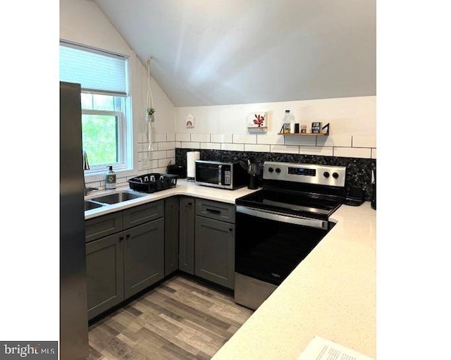 kitchen with hardwood / wood-style flooring, stainless steel appliances, backsplash, vaulted ceiling, and gray cabinets