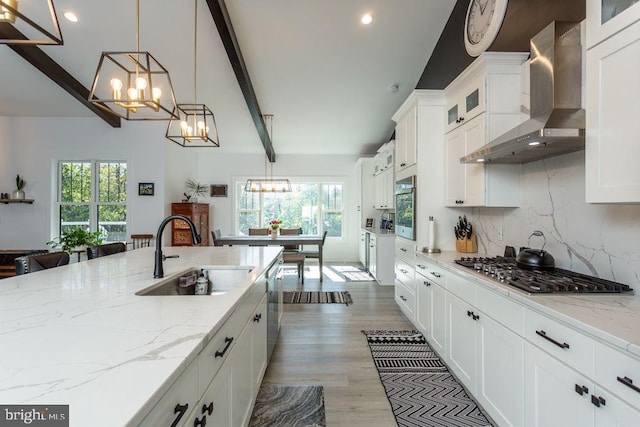 kitchen with white cabinets, beamed ceiling, pendant lighting, wall chimney exhaust hood, and sink