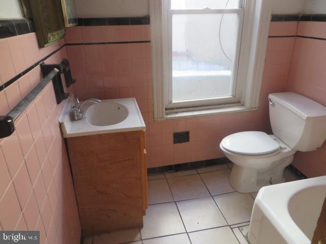 bathroom featuring a tub to relax in, toilet, tile patterned flooring, tile walls, and vanity