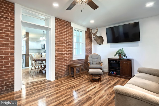 living room featuring hardwood / wood-style floors, ceiling fan, and brick wall