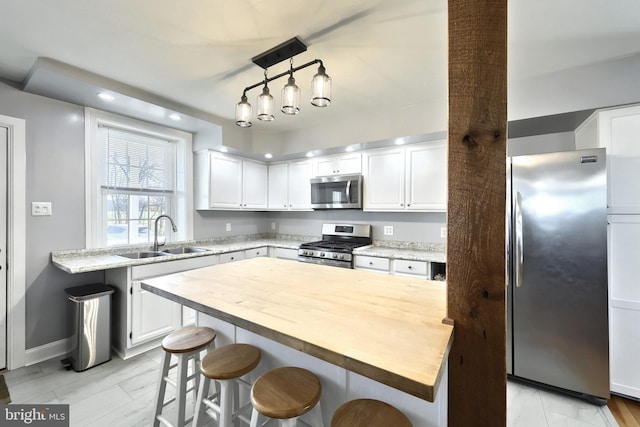 kitchen with pendant lighting, sink, a kitchen breakfast bar, white cabinetry, and appliances with stainless steel finishes