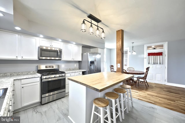 kitchen featuring stainless steel appliances, a breakfast bar area, a kitchen island, white cabinets, and butcher block countertops