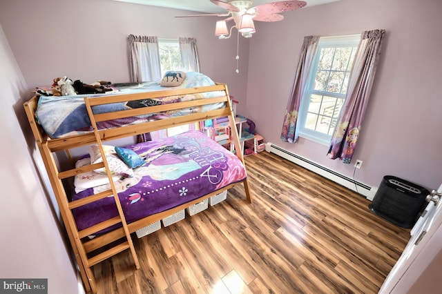 bedroom with baseboard heating, hardwood / wood-style floors, multiple windows, and ceiling fan