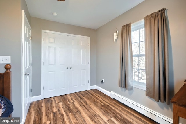 bedroom featuring baseboard heating, wood-type flooring, and a closet