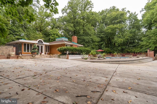 view of front of house with a patio area, a chimney, fence, and an outdoor pool