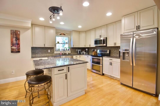 kitchen with appliances with stainless steel finishes, a kitchen breakfast bar, dark stone counters, decorative backsplash, and light hardwood / wood-style flooring