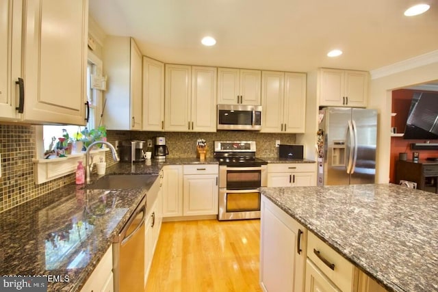 kitchen featuring sink, appliances with stainless steel finishes, light hardwood / wood-style floors, and dark stone counters