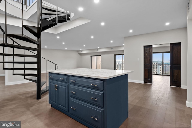 kitchen with a kitchen island, blue cabinetry, light stone countertops, and dark hardwood / wood-style floors