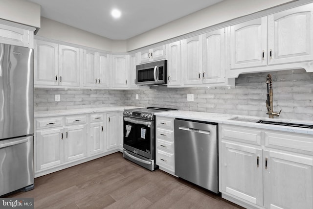 kitchen with hardwood / wood-style flooring, white cabinetry, sink, appliances with stainless steel finishes, and backsplash