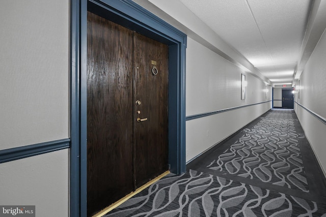 corridor featuring dark colored carpet and a textured ceiling