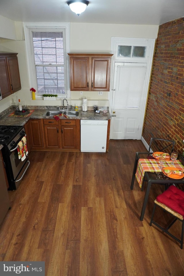 kitchen with dark hardwood / wood-style floors, stainless steel range, white dishwasher, brick wall, and sink