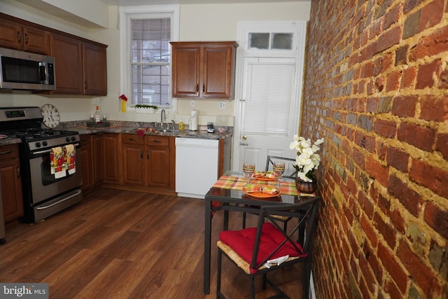 kitchen featuring appliances with stainless steel finishes, sink, dark stone counters, brick wall, and dark hardwood / wood-style floors