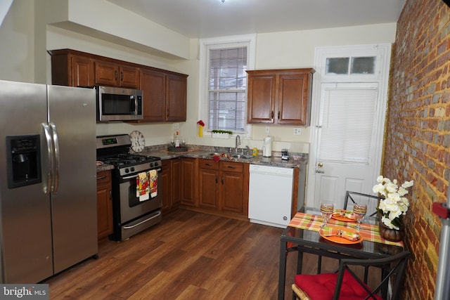 kitchen with dark hardwood / wood-style flooring, appliances with stainless steel finishes, dark stone countertops, sink, and brick wall