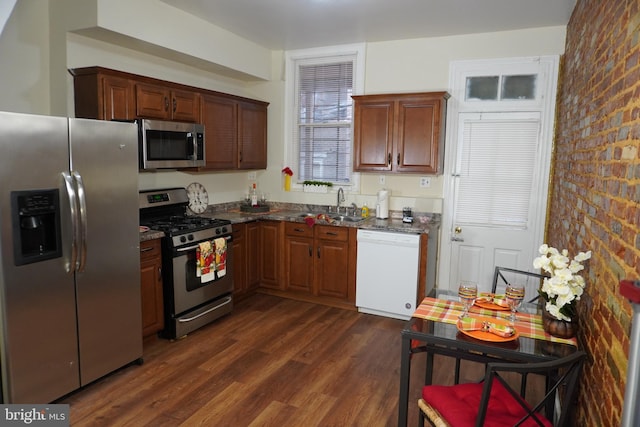 kitchen with appliances with stainless steel finishes, sink, dark stone countertops, brick wall, and dark hardwood / wood-style floors